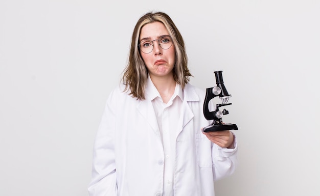 Jolie femme caucasienne se sentant triste et geignarde avec un regard malheureux et un scientifique qui pleure avec un concept de microscope