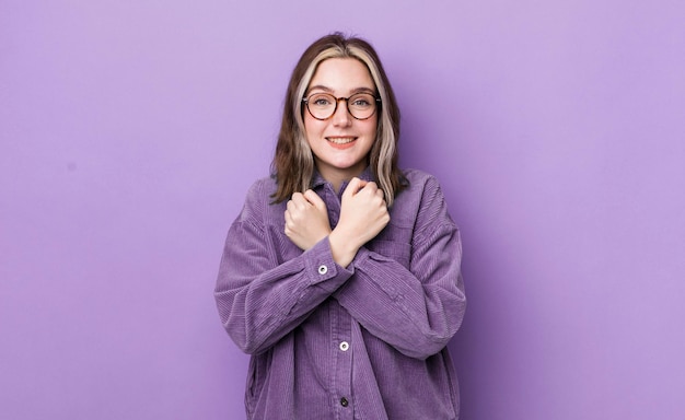 Jolie femme caucasienne souriant joyeusement et célébrant avec les poings serrés et les bras croisés se sentant heureux et positif