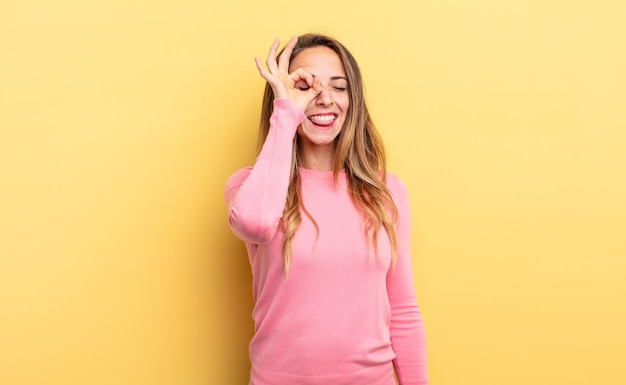 Jolie femme caucasienne souriant joyeusement avec un visage drôle, plaisantant et regardant à travers le judas, espionnant les secrets