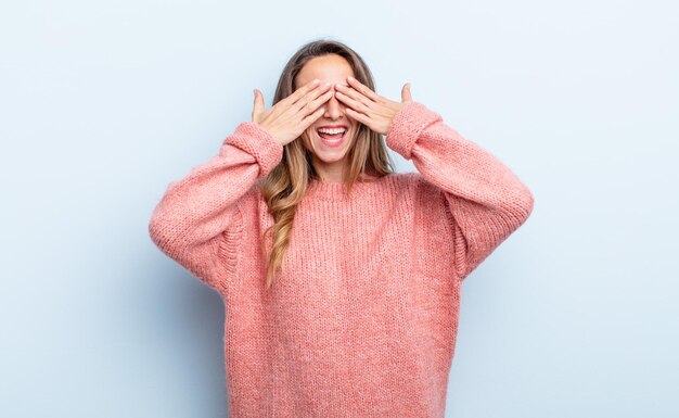 Jolie femme caucasienne souriante et se sentant heureuse, couvrant les yeux des deux mains et attendant une surprise incroyable