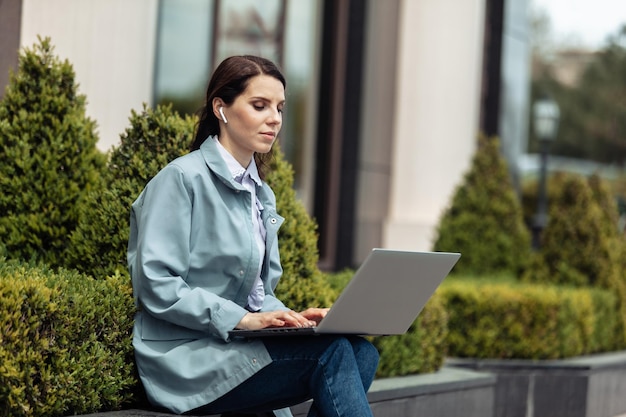 Jolie femme caucasienne utilise un ordinateur portable dans la ville à l'extérieur Travail à distance Femme d'affaires moderne