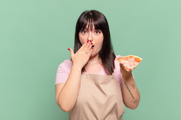 Jolie femme chef avec une expression effrayée et tenant une pizza