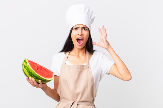 Jolie femme chef hispanique criant avec les mains en l'air et tenant une pastèque