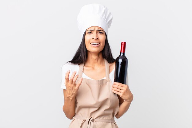 Jolie femme chef hispanique à la recherche désespérée, frustrée et stressée et tenant une bouteille de vin