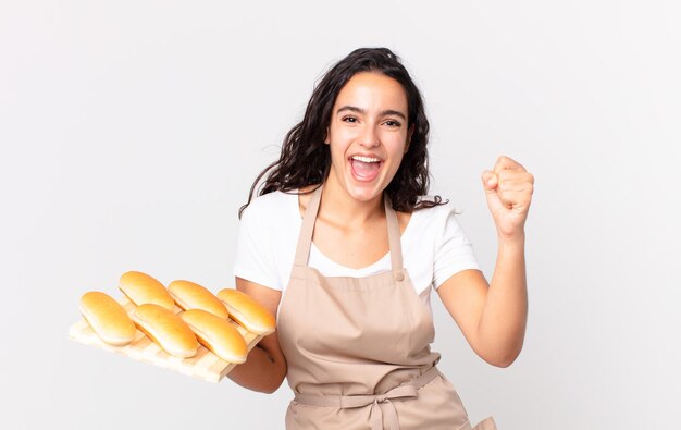 Jolie femme chef hispanique se sentant choquée, riant et célébrant le succès et tenant un pain troy