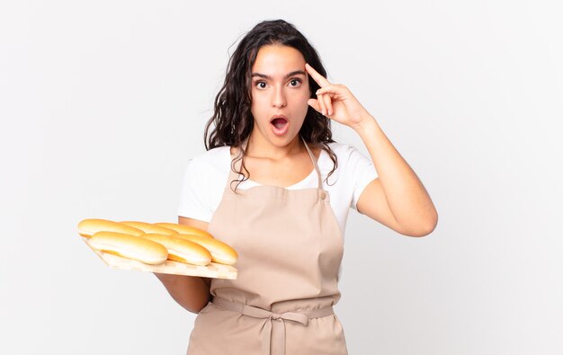 Jolie femme chef hispanique à la surprise, réalisant une nouvelle pensée, idée ou concept et tenant un pain troy