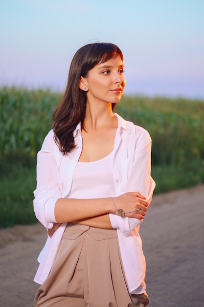 Jolie femme en chemise blanche posant sur une route de campagne au coucher du soleil