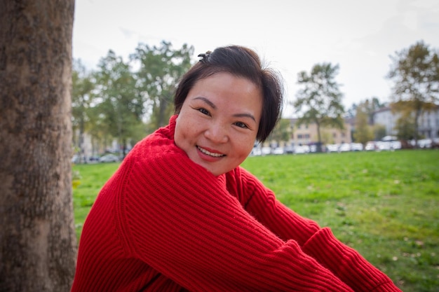 Jolie femme chinoise d'âge moyen souriante assise sur l'herbe dans le parc