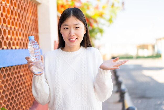 Jolie femme chinoise avec une bouteille d'eau à l'extérieur avec une expression faciale choquée