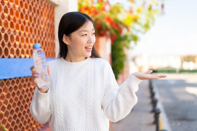 Jolie femme chinoise avec une bouteille d'eau à l'extérieur avec une expression faciale surprise