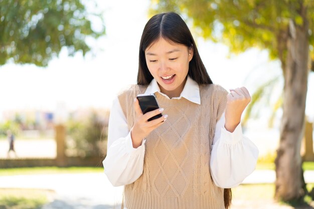 Jolie femme chinoise à l'extérieur surprise et envoyant un message