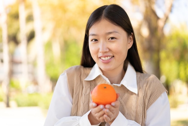 Jolie femme chinoise à l'extérieur tenant une orange avec une expression heureuse