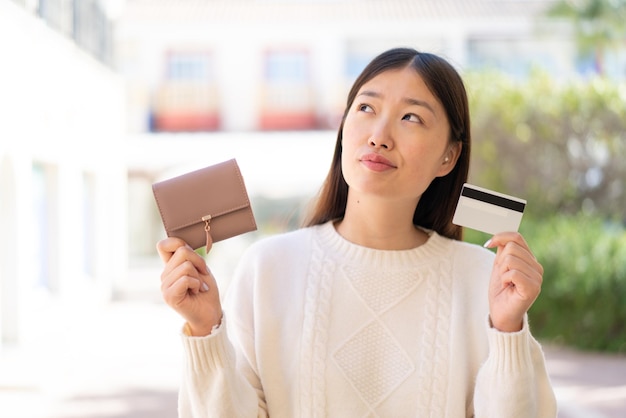 Jolie femme chinoise à l'extérieur tenant un portefeuille et une carte de crédit