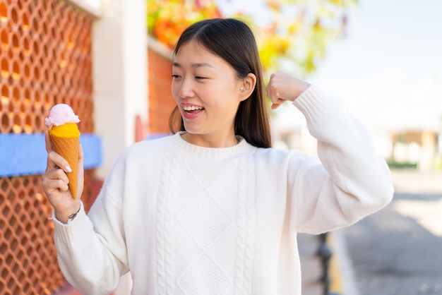 Jolie femme chinoise avec une glace au cornet à l'extérieur célébrant une victoire