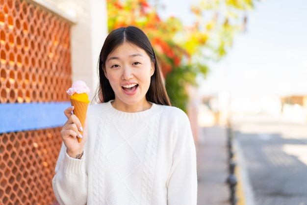 Jolie femme chinoise avec une glace au cornet à l'extérieur avec une expression faciale surprise et choquée