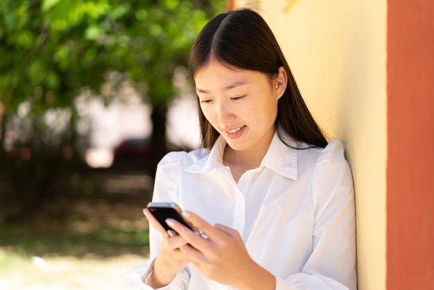 Jolie femme chinoise utilisant un téléphone portable à l'extérieur