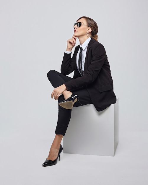 Jolie femme avec une coiffure rétro pose dans un costume et des lunettes de soleil pour hommes