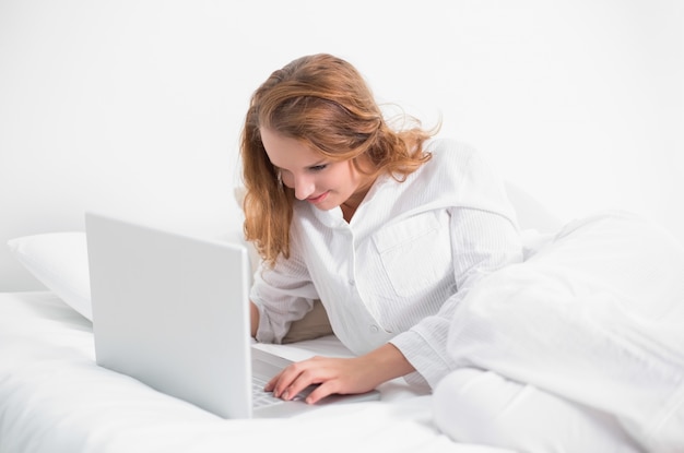 Jolie femme concentrée à l&#39;aide d&#39;un ordinateur portable allongé sur son lit