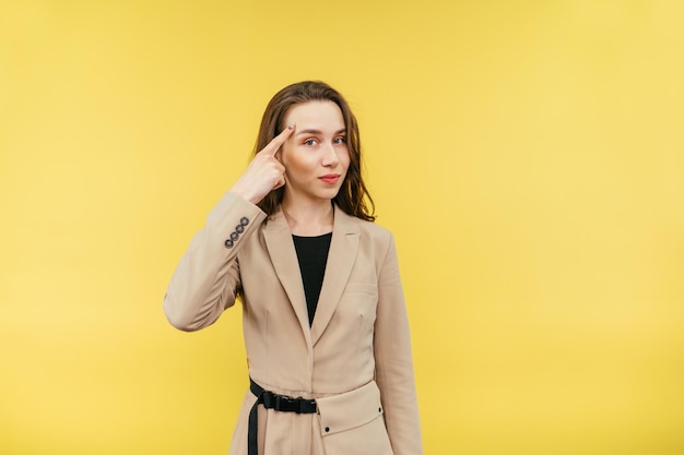 Jolie femme en costume beige se dresse sur un fond jaune et regarde la caméra