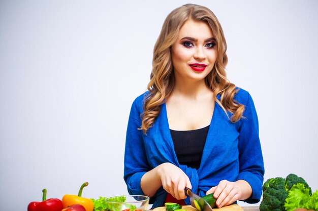 Une jolie femme coupe du concombre pour une salade diététique.