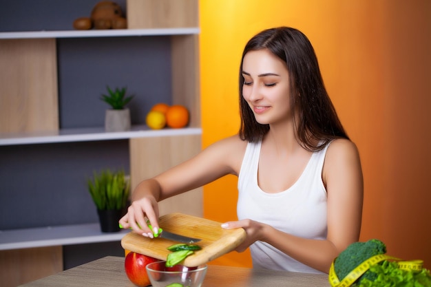 Une jolie femme coupe du concombre pour une salade diététique.