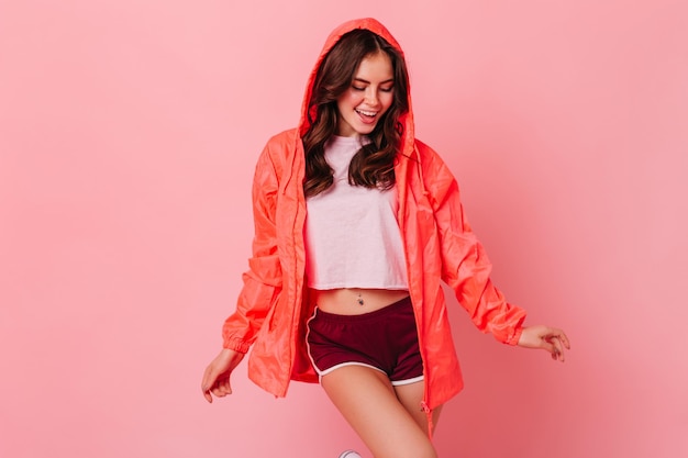 Jolie femme en coupe-vent lumineux avec sourire posant en studio rose sur fond isolé