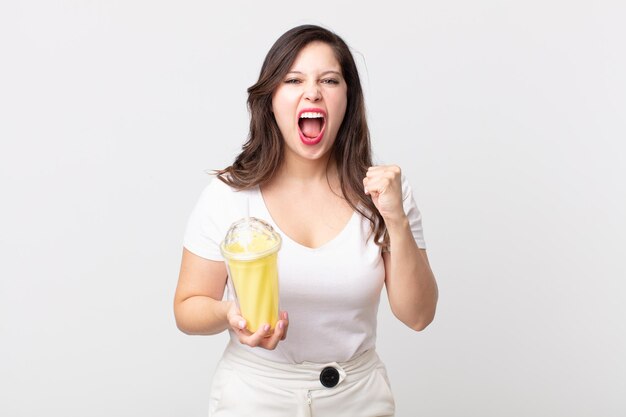 Jolie femme criant agressivement avec une expression de colère et tenant un milk-shake à la vanille