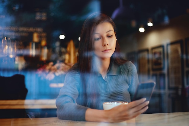 Jolie femme dans un café lisant quelque chose dans son téléphone portable