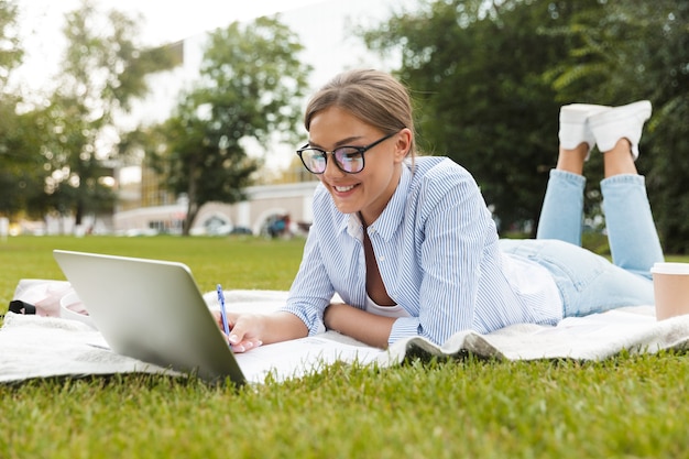 Jolie femme dans un parc à l'extérieur à l'aide d'un ordinateur portable par écrit