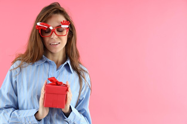 Jolie femme dans des verres de Noël détient une boîte-cadeau sur fond rose