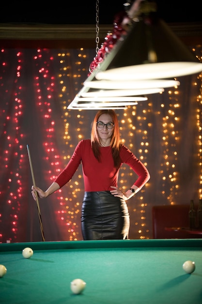 Une jolie femme debout dans un club de billard tenant une queue posant pour la caméra