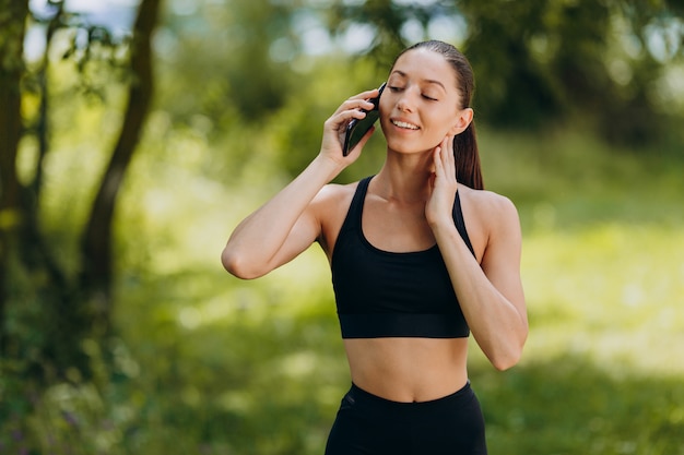 Jolie femme debout dans le parc et parler d'un smartphone en plein air.