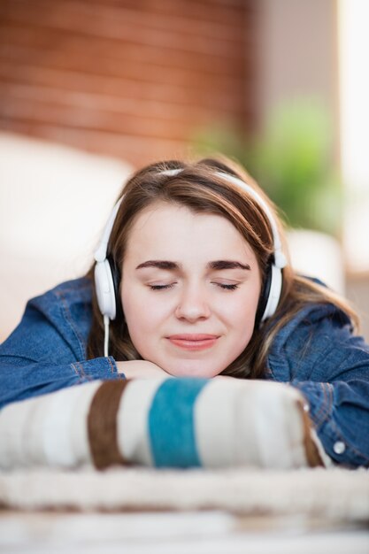 Jolie femme écoutant de la musique allongée sur le sol dans le salon