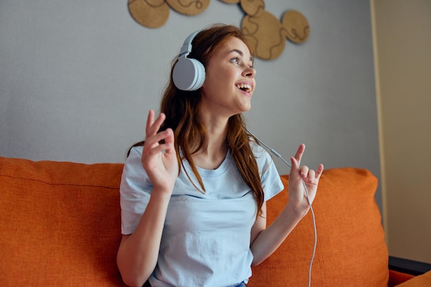 jolie femme écoutant de la musique avec des écouteurs sur le canapé orange des appartements photo de haute qualité