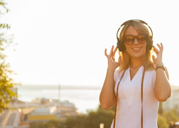 Jolie femme écouter de la musique dans les écouteurs dans les rayons du soleil au lever du soleil