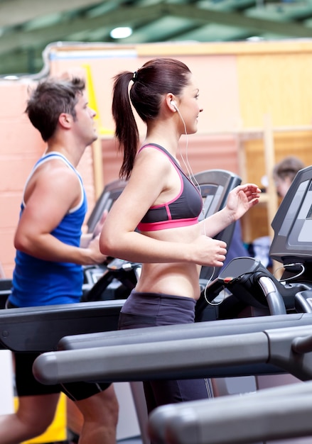Jolie femme avec des écouteurs à l&#39;aide d&#39;un tapis roulant avec son petit ami dans un centre de fitness