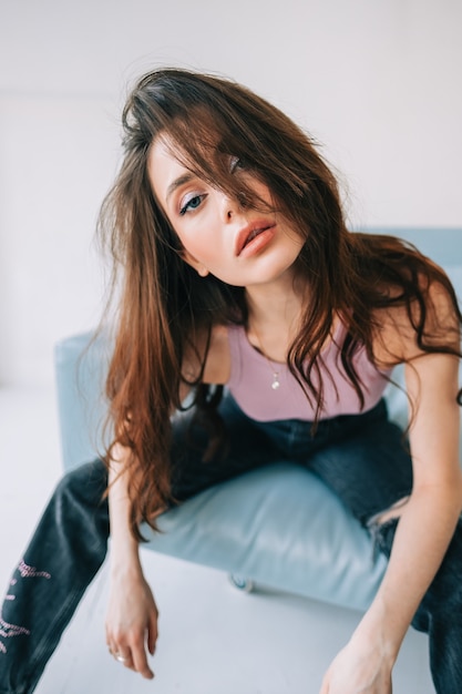 Photo jolie femme élégante avec de longs cheveux brune posant sur un canapé bleu dans un salon moderne