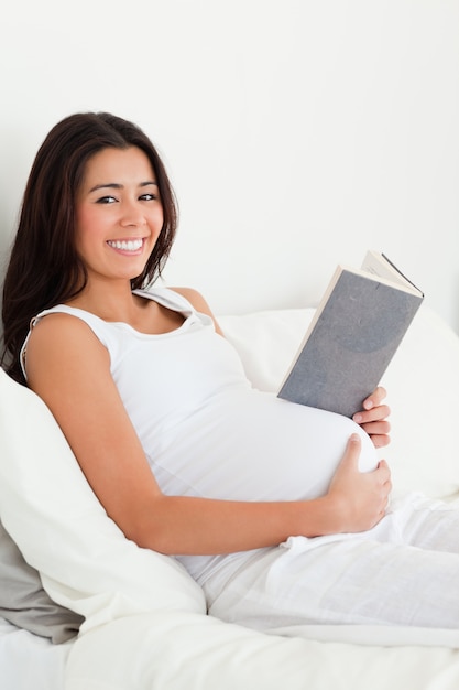 Jolie femme enceinte lisant un livre en position couchée sur un lit