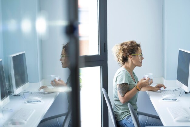 Une jolie femme entrepreneur professionnelle travaillant sur ordinateur et buvant du café dans l'activité professionnelle du matin Lieu de travail de bureau blanc brillant Femmes modernes assises au bureau et lisant en ligne