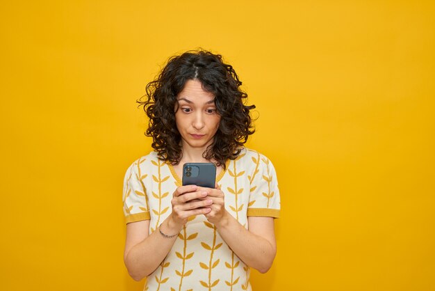 Jolie femme envoyant des SMS sur son téléphone. Elle a l'air très surprise, regardant le téléphone portable qu'elle tient à deux mains.