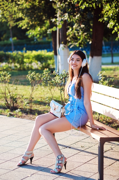 Jolie femme est assise sur le banc dans le parc et écoute de la musique.