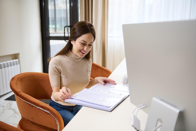 Jolie femme européenne examinant un dossier avec des documents assis dans le fauteuil dans un immeuble de bureaux moderne