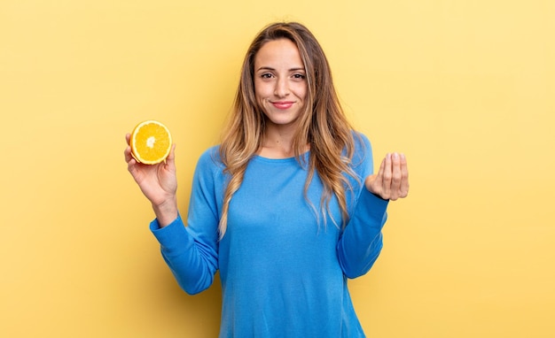 Jolie femme faisant un capice ou un geste d'argent vous disant de payer en tenant une demi-orange