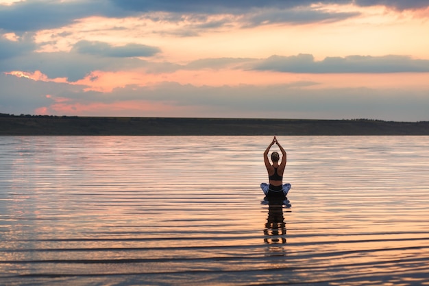 La jolie femme faisant du yoga au coucher du soleil à l'extérieur