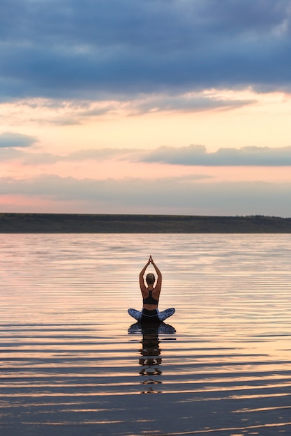 La jolie femme faisant du yoga au coucher du soleil à l'extérieur