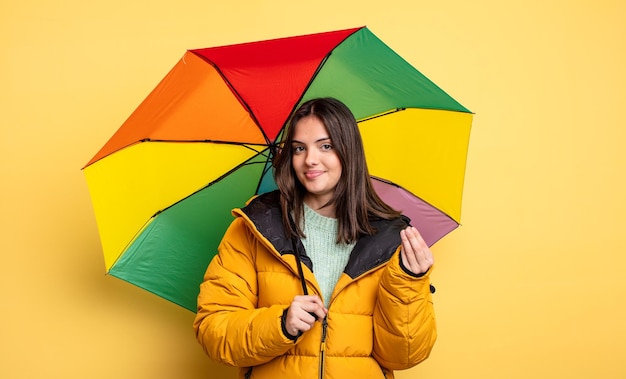 Jolie femme faisant un geste de capice ou d'argent, vous disant de payer. concept d'hiver et de parapluie