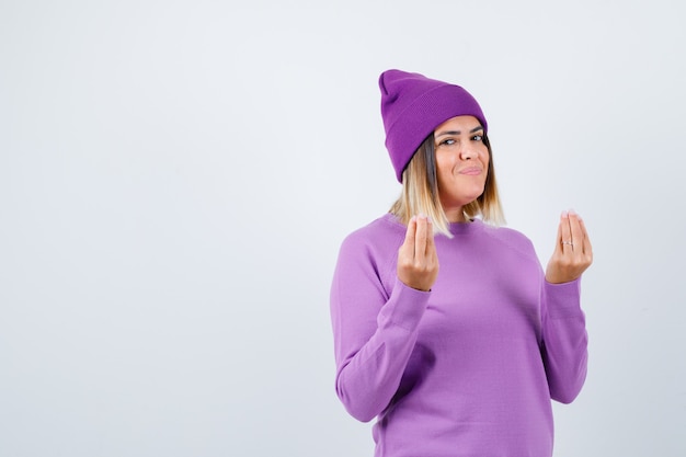 Photo jolie femme faisant un geste italien en pull, bonnet et à la gaieté, vue de face.