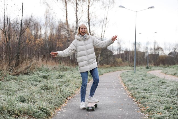 Une jolie femme faisant de la planche à roulettes dans un parc en automne, apprenant à faire du skateboard passant le week-end à l'air frais à l'extérieur. Concept de sport sain.