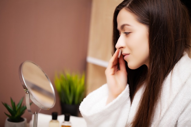 Jolie femme faisant des procédures cosmétiques à la maison devant le miroir