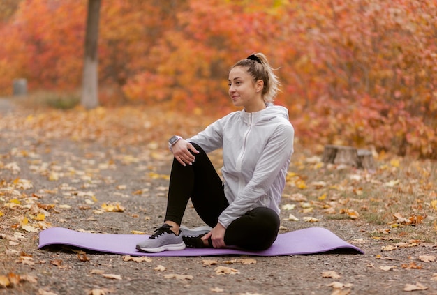 Une jolie femme en forme est assise sur un tapis dans la forêt d'automne